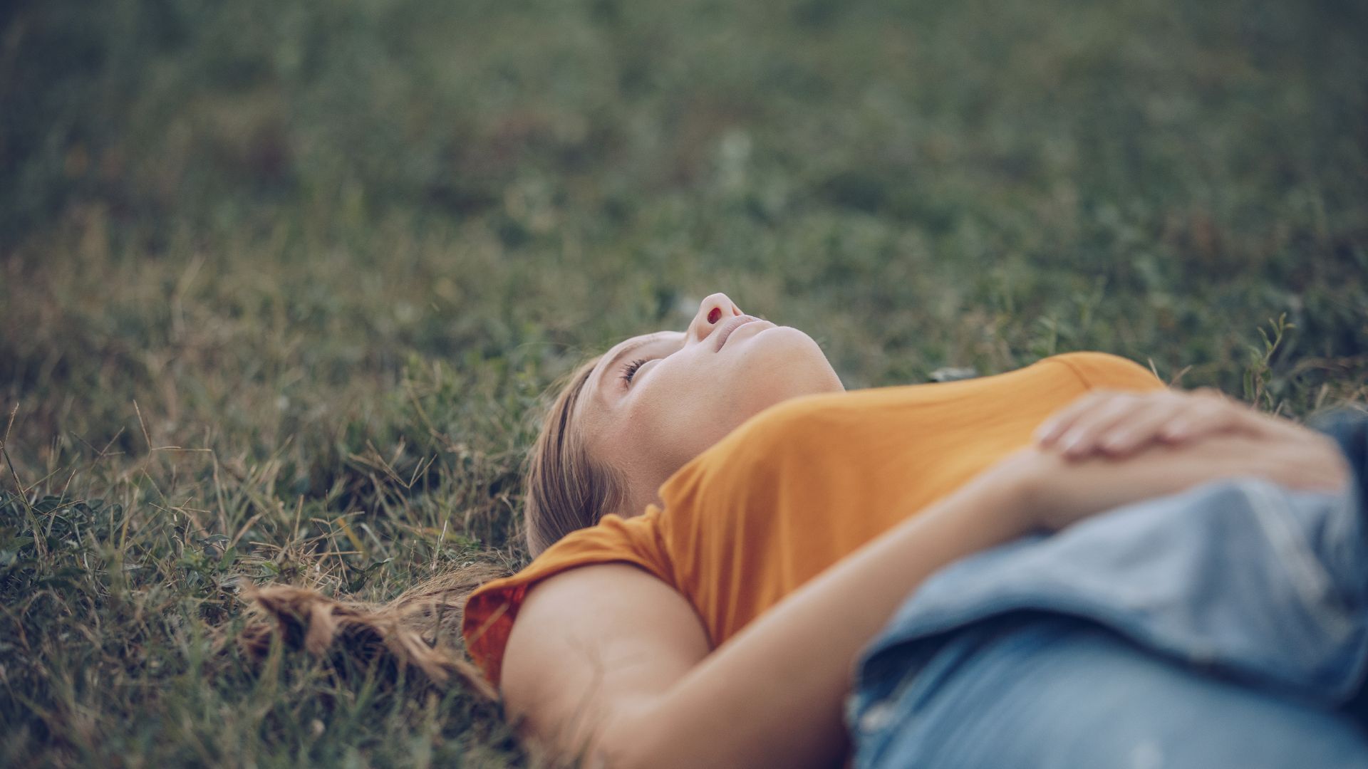 A woman lying in grass, appearing relaxed and at peace, symbolizing the positive impact of effective mental health care and medication management. REACH Ohio