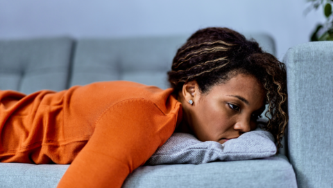 A woman lying on a couch, looking contemplative, representing the challenges of mental health. Is depression a disability? This article explores how severe depression can impact daily life and available support options. REACH, OHIO