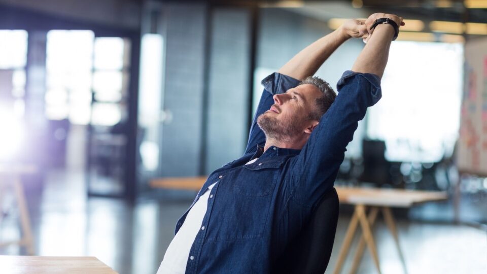 A man sitting in a chair with his hands up, symbolizing relief and openness during ketamine therapy, which can treat conditions like depression, anxiety, and PTSD. REACH, Ohio