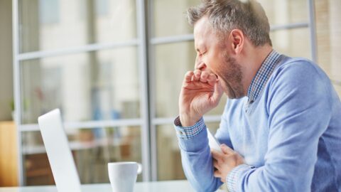 A tired man yawning and covering his mouth with his hand, showing the effects of dealing with insomnia.