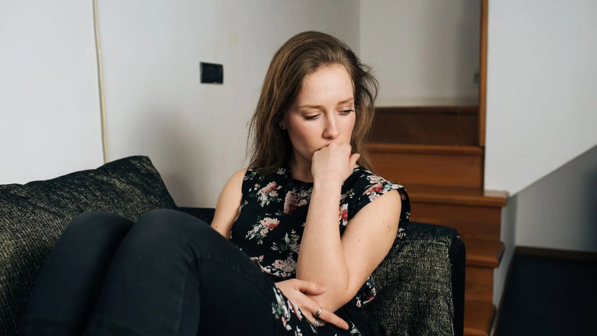 A young woman sitting on a couch, looking down and appearing deep in thought, reflecting emotional distress—ideal for illustrating self-reflection in a mental health context: Do I have BPD or am I BPD?