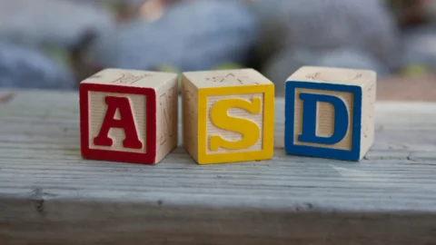 Wooden alphabet blocks displaying the letters A, S, and D sitting on a wooden surface, symbolizing an ADOS 2 assessment. Image accompanies a guide explaining what to expect during an ADOS-2 assessment for Modules 1, 2, and 3—highlighting that the ADOS-2 is a relaxed, play-based session designed to understand communication, behavior, and social interaction without pressure or testing, and pointing families toward learning more about autism evaluations at REACH.