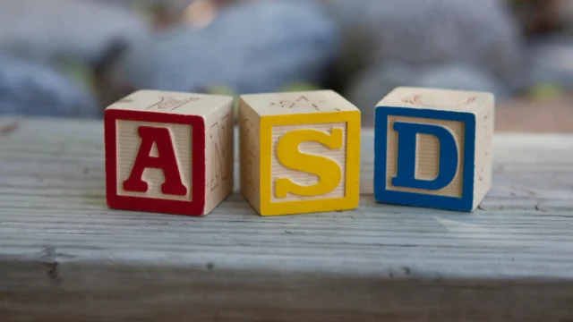 Wooden alphabet blocks displaying the letters A, S, and D sitting on a wooden surface, symbolizing an ADOS 2 assessment. Image accompanies a guide explaining what to expect during an ADOS-2 assessment for Modules 1, 2, and 3—highlighting that the ADOS-2 is a relaxed, play-based session designed to understand communication, behavior, and social interaction without pressure or testing, and pointing families toward learning more about autism evaluations at REACH.