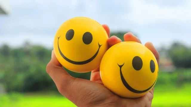 A hand squeezing two yellow smiley face stress balls outdoors — a common example of stimming behavior that illustrates what does stimming mean in everyday sensory regulation.