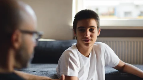 Teenage boy in a white T-shirt talking with an adult, illustrating the conversation-based approach of ADOS-2 modules 3 and 4. REACH behavioral health